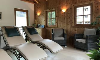 A cozy room with two loungers and wooden interior design. There are windows with a view outside and a relaxing atmosphere.