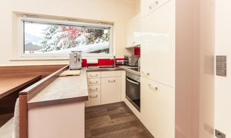 A modern kitchen with bright cabinets and red accents. Large windows offer a view of a snowy landscape.