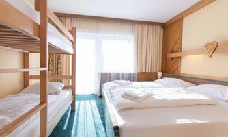 A bright hotel room with a double bed and a loft bed. Large windows let in plenty of daylight.