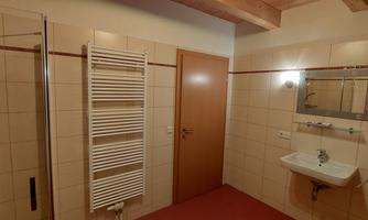 A simple bathroom with a shower, a sink, and a towel warmer. The walls are brightly tiled and there is a door to an additional room.
