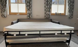 A comfortable sofa bed with a pull-out mattress is in a bright room. Large windows and elegant curtains create an inviting atmosphere.