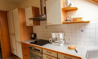 A modern kitchen with wooden cabinets and a stone countertop. On the table, there is a coffee pot and fresh bread.