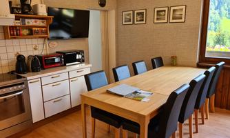 A cozy kitchen with a large dining table and several chairs. The walls are decorated, and the room has plenty of natural light.