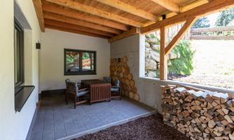 A cozy terrace with wooden chairs and a small table. Next to the terrace is stacked firewood.