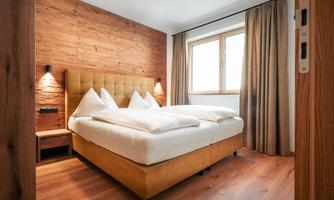 A modern bedroom with a cozy double bed and warm wooden walls. Large windows let in plenty of light and create an inviting atmosphere.