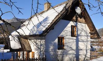 A cozy house with a snow-covered roof. It stands in a snowy landscape under clear, blue sky.