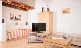 A cozy living space with a television and a wooden table. The walls are light, and there is a rustic piece of furniture as well as a cozy seating area.
