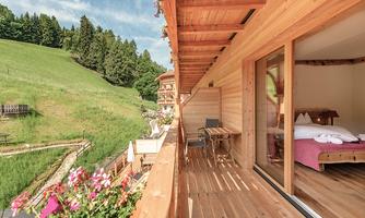 A cozy balcony with wooden decoration and a view of green meadows and trees. There are chairs on the table, perfect for relaxing in nature.