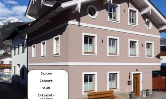 A modern building with a bright facade and a cozy garden. In front of the house, there is a bench and there are amenities such as Wi-Fi and infrared cabins.