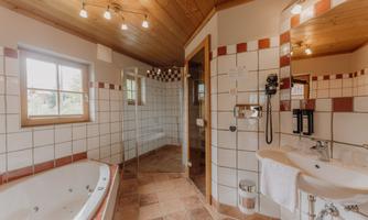 A spacious bathroom with a bathtub and a glass shower. White tiles and wooden details create an inviting atmosphere.