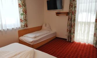 A simple room with two beds and a television on the wall. The windows are adorned with curtains and provide plenty of natural light.