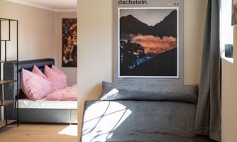 A cozy living space with a gray sofa and a wooden table. In the background, there are two beds with pink pillows and a piece of artwork on the wall.