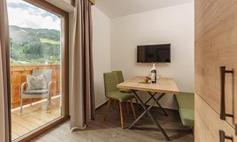 A cozy dining area with a view of the mountains. The room is bright and modernly furnished, with a table, chairs, and a television.