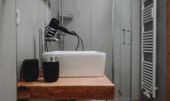 A modern bathroom with a white sink and a hairdryer. In the background, a shower and towel holders are visible.