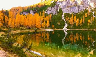 A picturesque lake with clear water and colorful, autumnal trees in the background. The mountains are beautifully reflected on the surface of the water.