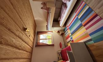 A cozy children's room with a colorful rug and a loft bed. The room has wooden details and a bright window front.