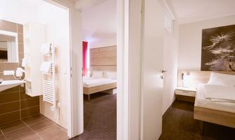 A modern hotel room with two beds and an adjoining bathroom. The decor is simple and bright, with a friendly atmosphere.