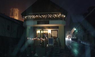 A cozy building with a brightly lit facade and Christmas lights. It is night and the snow is on the ground.