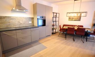 A modern kitchen with gray cabinets and an adjoining dining area. The dining area is furnished with a table and red chairs.