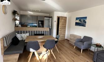 A modern living room with an open kitchen. The space is bright and friendly, with a dining table and comfortable seating.