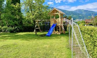 A beautiful garden with a play tower and a slide. In the background, there is a soccer goal and the mountains are visible.