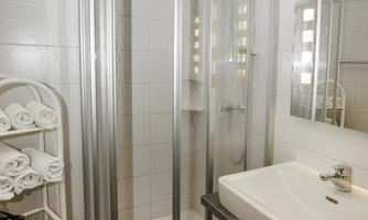 A modern bathroom with a shower and sink. Fresh towels are ready on a shelf.