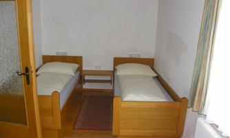 A simple bedroom with two wooden single beds. There is a small table and a window with curtains.