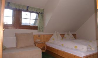 A cozy bedroom with a single bed and a seating area. Large windows provide plenty of daylight and a pleasant atmosphere.