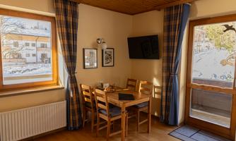 A cozy dining area with a table and chairs in a bright room. A wintry landscape is visible through the windows.