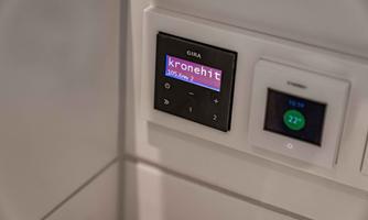 A modern control panel with a display showing the radio station "kronehit". Next to it is another control panel for temperature regulation.