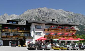 A chalet in alpine style with balconies and red sunshades. In the background, majestic mountains rise under a clear sky.