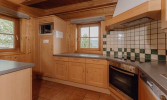 A cozy kitchen with wooden elements and large windows. The walls are adorned with green and white tiles.