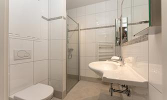 A modern bathroom with white tiles. It features a shower, a sink, and a toilet.