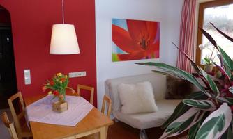 A cozy living area with a dining table, a couch, and colorful decorations. On the wall hangs a large, colorful picture of a flower.