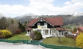 A charming house with a red roof and a large terrace. It is picturesquely located in a green landscape with mountains in the background.