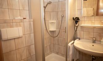 A modern bathroom with a shower and a sink. The walls are tiled and there is a practical towel holder.