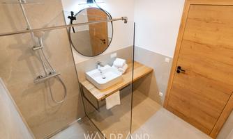 A modern bathroom with a shower and a stylish sink. The walls are bright and the wooden details add a warm touch.