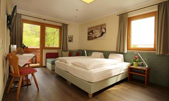 A bright room with two beds and a small table.  
Large windows offer a view outside and provide plenty of daylight.