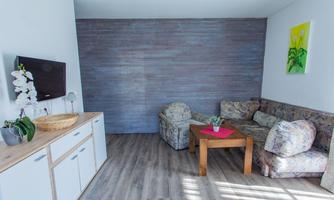 A bright living room with a television and a modern sideboard. The furniture is comfortable and includes a patterned couch and a wooden table.