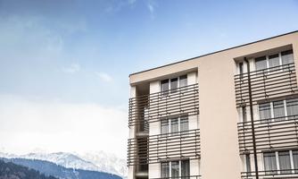 A modern building with large windows and a clear blue sky. Snow-capped mountains can be seen in the background.