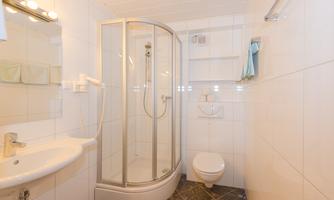 A modern bathroom with a shower cabin, sink, and toilet. The walls are tiled and the lighting is bright.