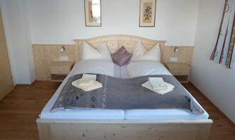 A cozy bedroom with a double bed made of light wood. The walls are simple and adorned with decorative pictures.