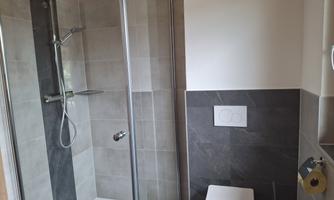 A modern bathroom with a shower and a toilet. The walls are decorated with gray tiles.