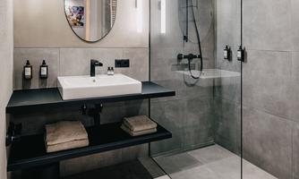 A modern bathroom with a glass shower enclosure and an elegant sink arrangement. The walls are in neutral shades of gray, and the lighting creates a pleasant atmosphere.