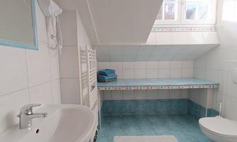 A modern bathroom with a sink, a toilet, and a towel rack. The walls are tiled white, and there are blue towels on the shelf.