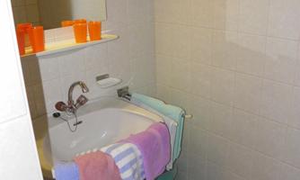 A small bathroom with a bathtub and colorful towels. On a shelf, there are orange cups and a green bowl.