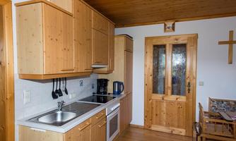 A modern kitchen with wooden cabinets and a blue coffee pot. The room has a friendly atmosphere and a door made of glass and wood.