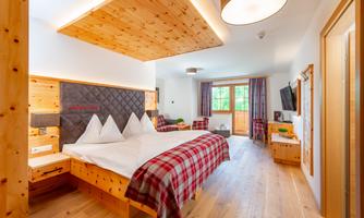 A modern bedroom with wood decor and a large bed. The room has windows overlooking the outdoors and a cozy atmosphere.