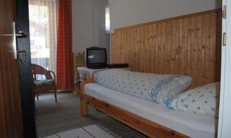 A simple room with a single bed and a seating area. The room has wooden paneling and a window with curtains.