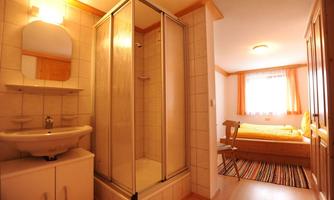 A modern bathroom with a shower and a sink. In the background, a cozy bedroom with a large window can be seen.